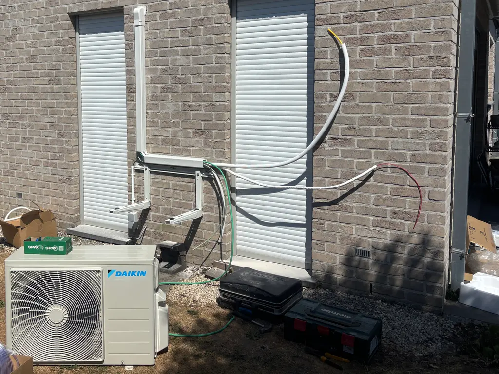 Wandbeugel hangt tegen de gevel, de koelleidingen worden doorgetrokken en de buitenunit staat nog op het gras.
